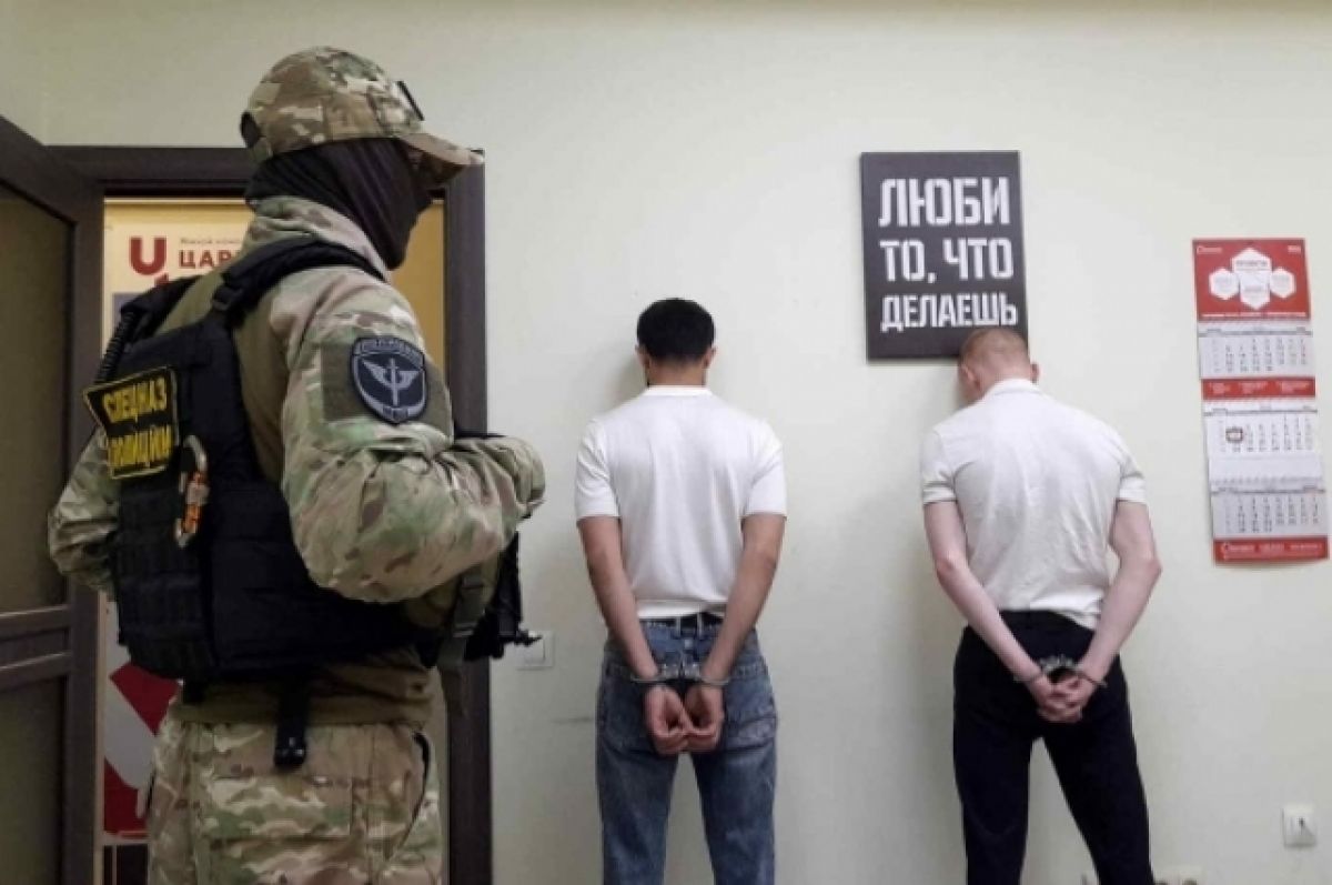 Человек в форме рядом с двумя мужчинами, стоящими лицом к стене.